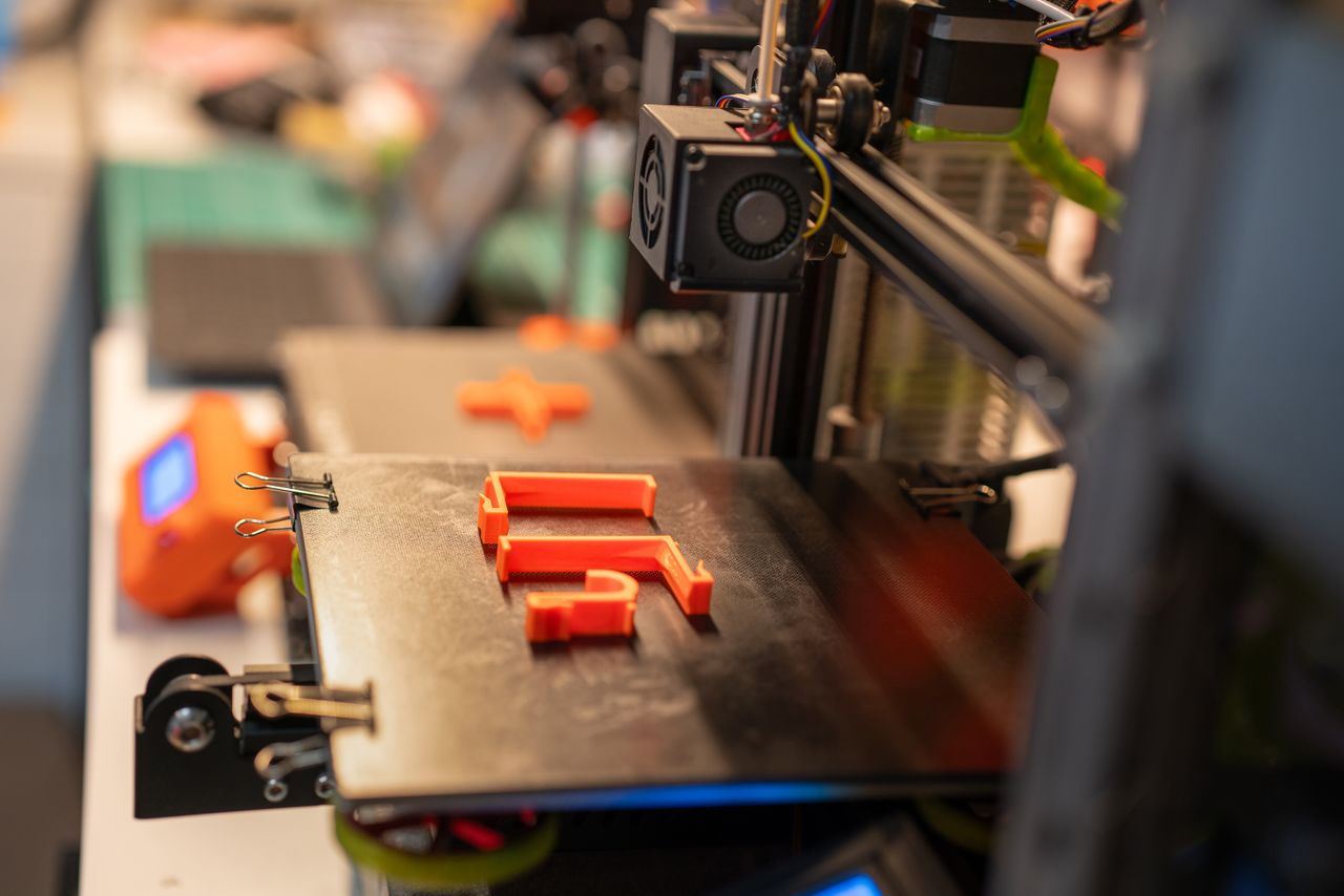 The Art of Drawing Readers In: Your attractive post title goes here Detailed view of a 3D printer creating an orange plastic part showcasing advanced technology.
