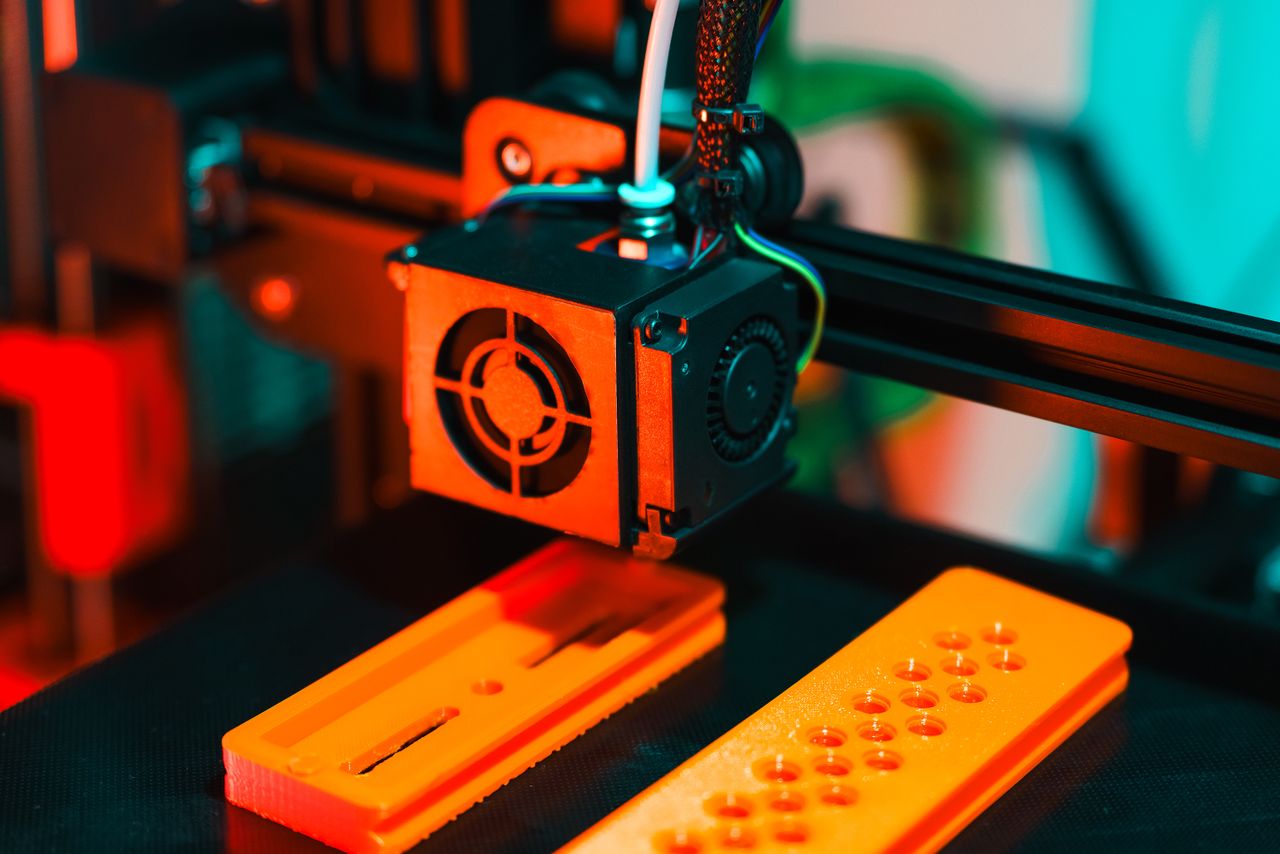 Crafting Captivating Headlines: Your awesome post title goes here Detailed view of a 3D printer in action, extruding orange plastic components.
